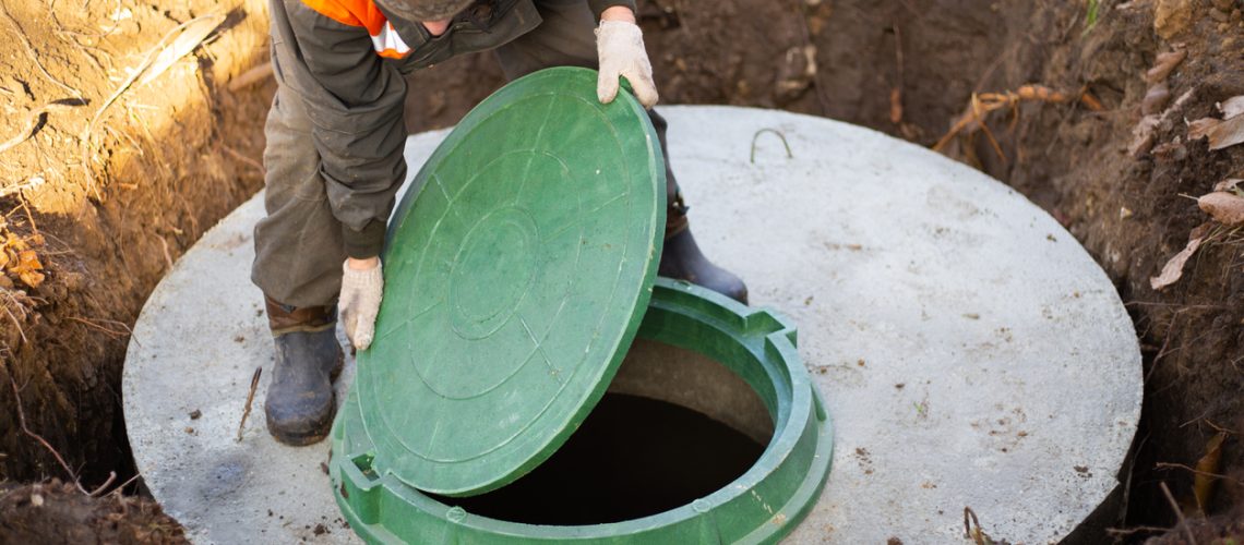 A worker installs a sewer manhole on a septic tank made of concrete rings. Construction of sewerage networks for country houses.